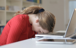 Photo of exhausted woman with her forehead resting on the edge of her laptop