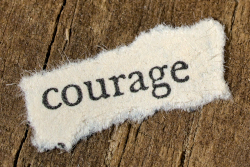 Photo of a scrap of paper with the typewritten word "courage" laid on a wooden background