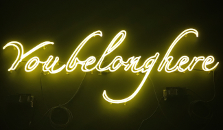 Photo of a neon sign on a black background reading "You belong here" in script.