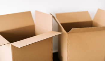 Photo of brown cardboard packing boxes, top flaps open, against a white wall.