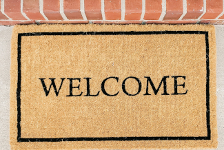 Photo of a doormat reading WELCOME in front of a red-brick step.
