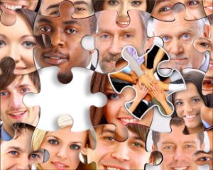 A jigsaw puzzle collage of multi-racial, multi-generational faces; one piece is pulled out and shows a group of hands clasped in the center.