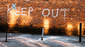 Photo of a brick wall with white graffiti spelling KEEP OUT, lit from below with lamps along the concrete roadway.