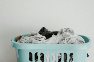 Photo of a light teal green laundry basket piled with clothes.