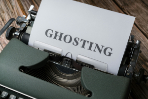 Closeup photo of a dark gray typewriter with a white sheet of paper in it that reads GHOSTING