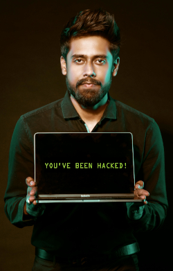 Photo of a man in dark green holding a laptop facing forward with the words "YOU'VE BEEN HACKED," on a dark background.