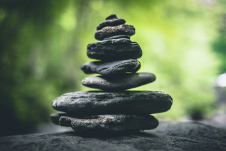 Photo of a pyramid pile of balanced flat rocks, with a soft-focus green growing things behind it.