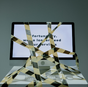 Photo fo a computer screen with crisscrossed caution tape all over it; behind the tape, the screen reads "unfortunately, we no longer need your services"
