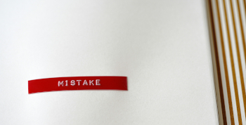 Photo of a red embossed label reading MISTAKE on a white background with brown-and-white vertical ridges on the right.